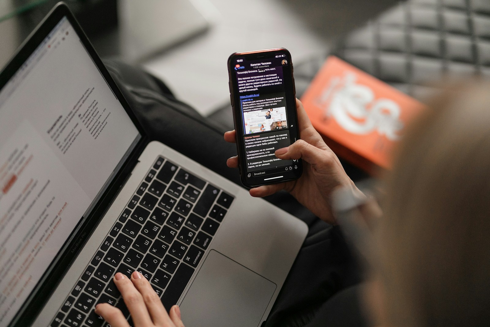Person reading a newsletter on a smartphone while working on a laptop